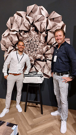 Pascal Versluis en Bob Looijschelder (rechts) van Textiles & More, staande op de mFLOR Parva Broad Leaf Warm Sycamore in visgraatpatroon. Op de achterwand het luxury print carpet. Pascal Versluis en Bob Looijschelder